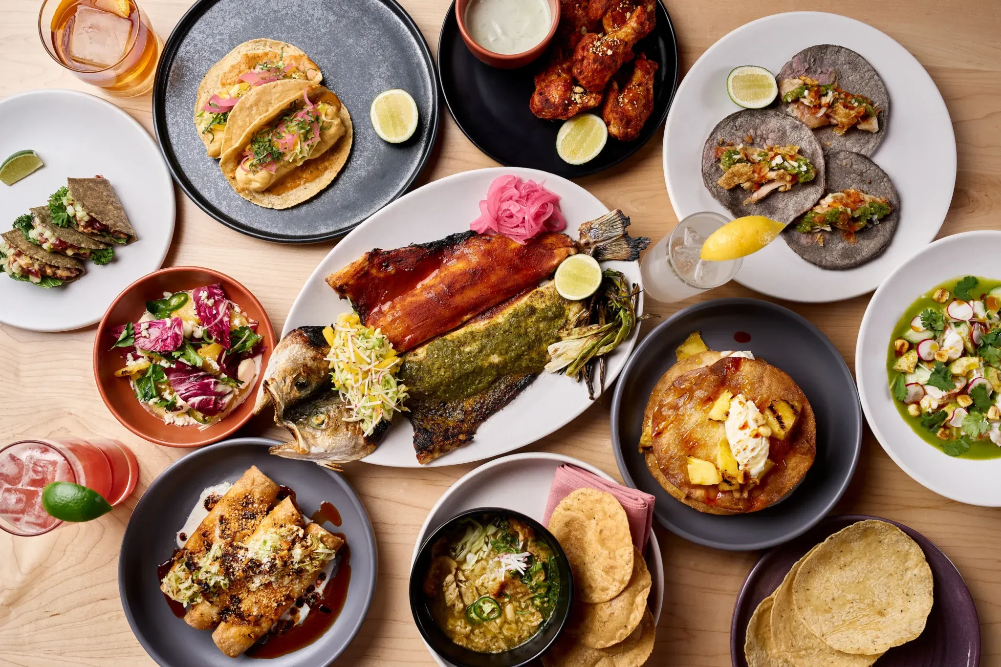 A spread of tacos, wings, whole fish, and salsas from above
