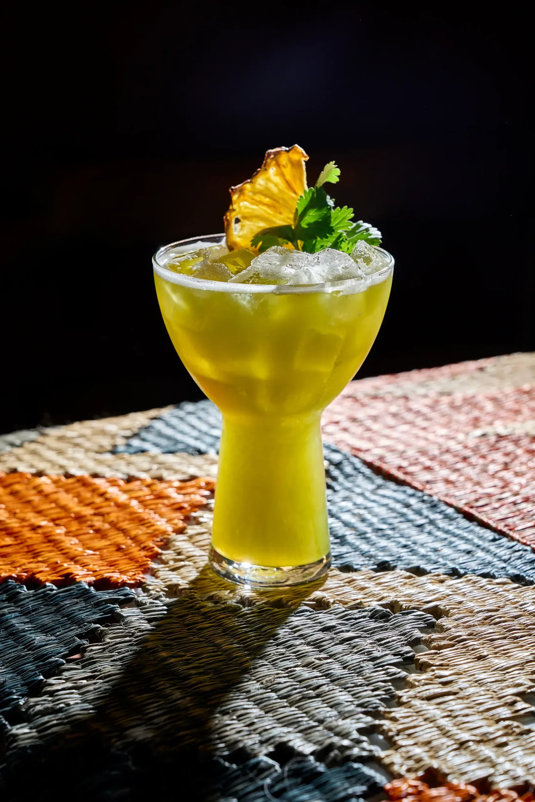 A pineapple-garnished cocktail on a woven runner