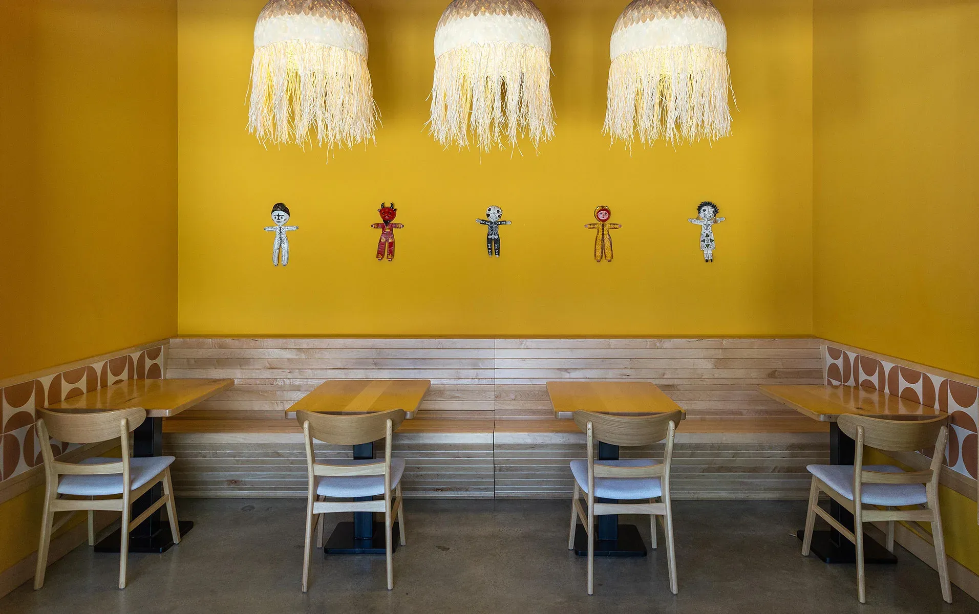 A sunlit yellow banquette in the dining room, set with woven light and muñecos